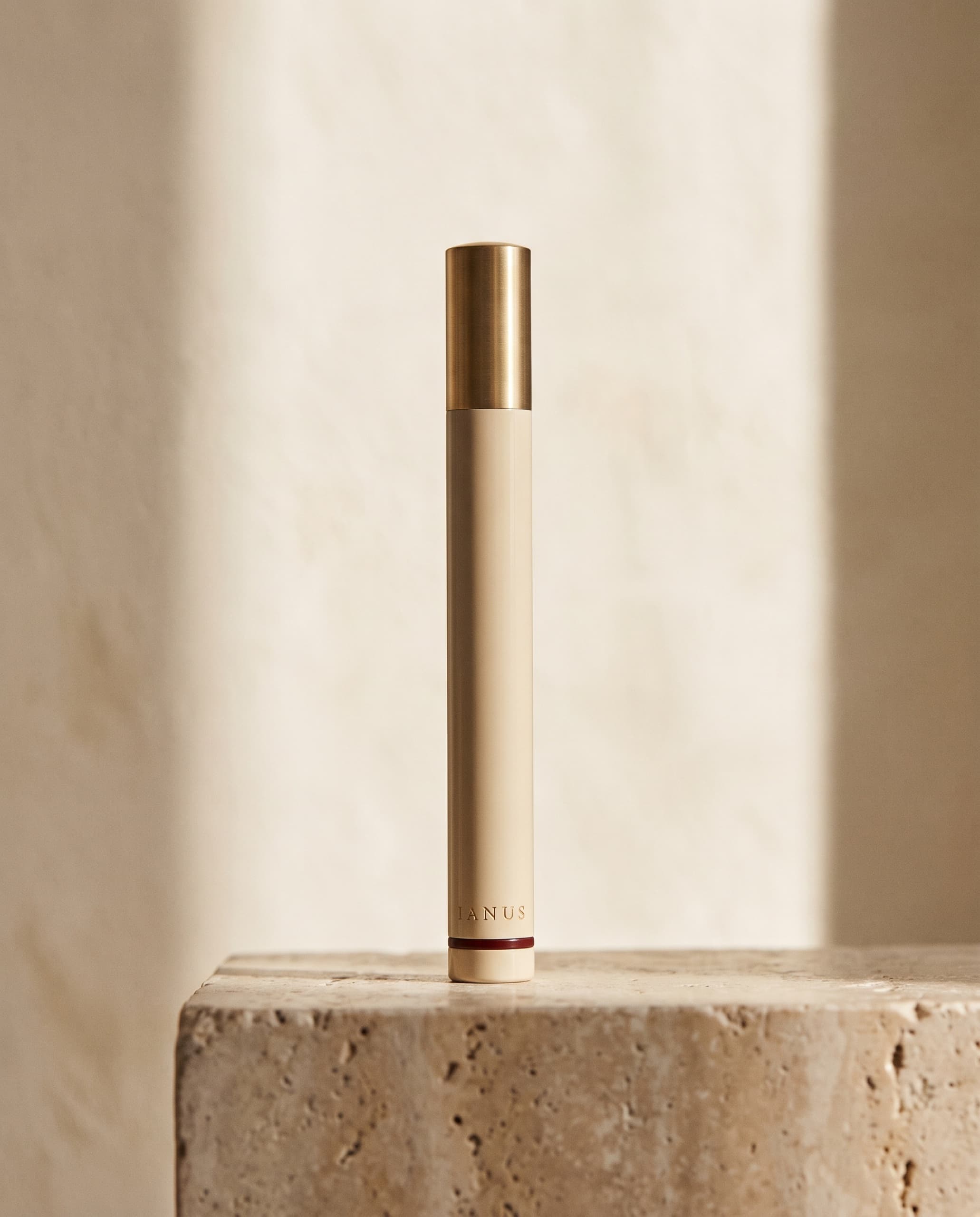 The IANUS press instrument — bone lacquer and brushed brass, standing on travertine